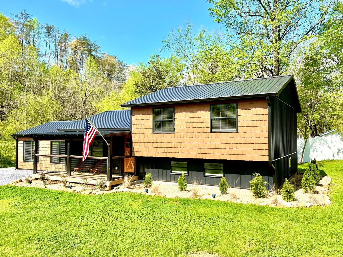 The front porch of the property is adorned with an American flag and bordered by a landscaped garden, offering a warm and welcoming entry that blends seamlessly with the surrounding natural beauty.