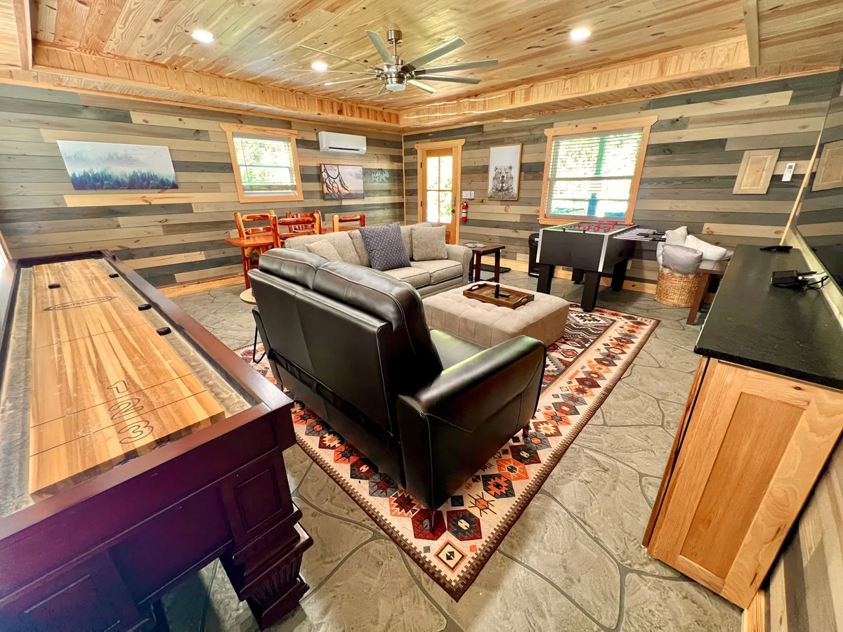 A welcoming entertainment space with a comfortable seating area, vibrant decorative rug, shuffleboard table, and foosball table. The arrangement encourages both relaxation and energetic gameplay.