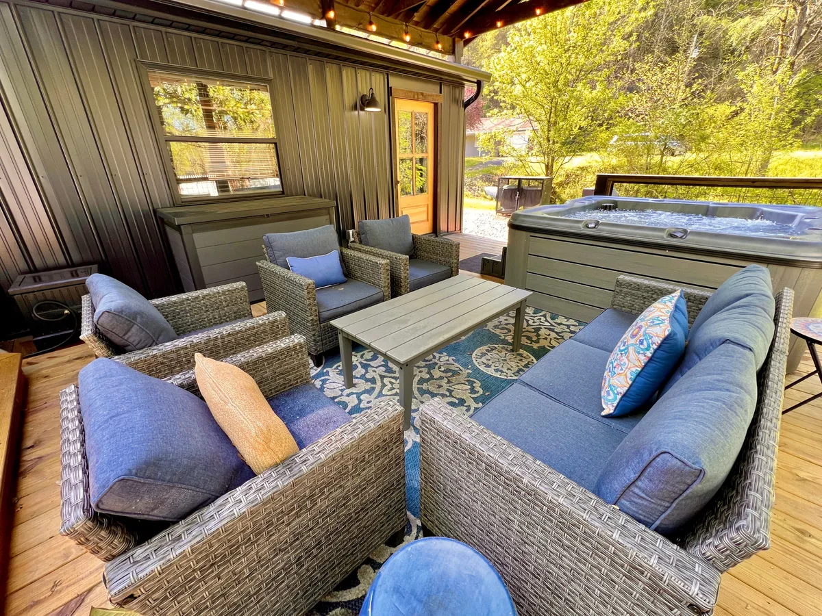 This exterior image features a cozy seating area and an inviting hot tub bordered by a decorative rug, setting the scene for relaxed group gatherings or evening chats under subtle lighting.
