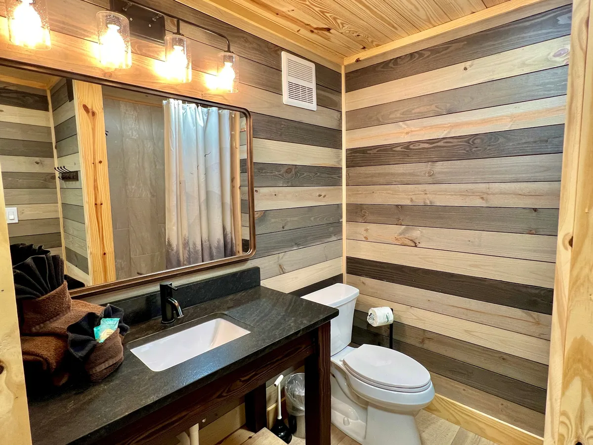 A stylish bathroom with wooden wall paneling, a vanity sink, a large mirror, and warm lighting fixtures. The ambiance is cozy and inviting, ideal for personal grooming and unwinding after a day of adventure.