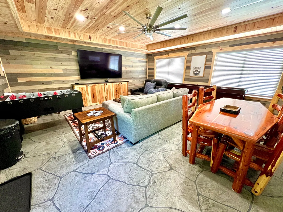 A spacious game room featuring a cozy sofa, a dining table perfect for board games, a foosball table, and a large television. The room is designed for comfort and lively gatherings, with ample space for various activities.