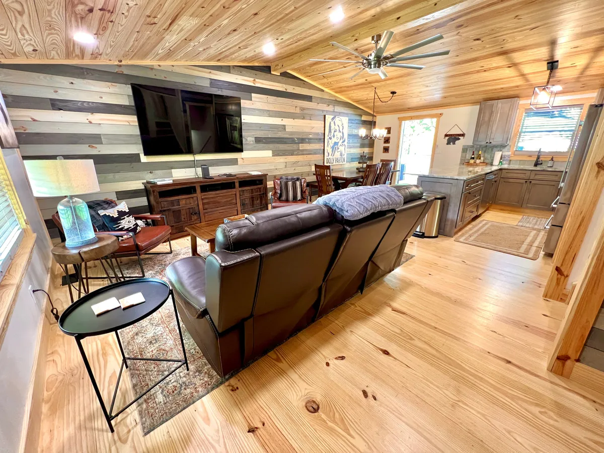 This image presents an inviting, open-concept space featuring a comfortable leather sofa, a wooden accent wall, a welcoming dining area, and a glimpse of the adjacent kitchen. The overall ambiance is warm and cohesive, capturing the heart of the living, dining, and kitchen areas together.