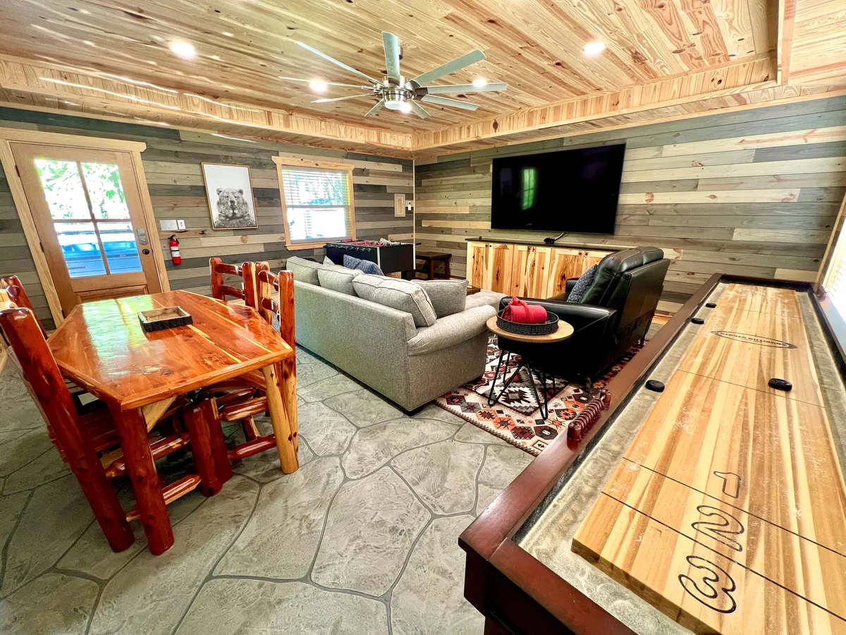 A spacious interior with a wooden dining table, comfortable sofa, large television, sliding door, and a shuffleboard table—capturing the essence of indoor group entertainment, games, and shared meals.