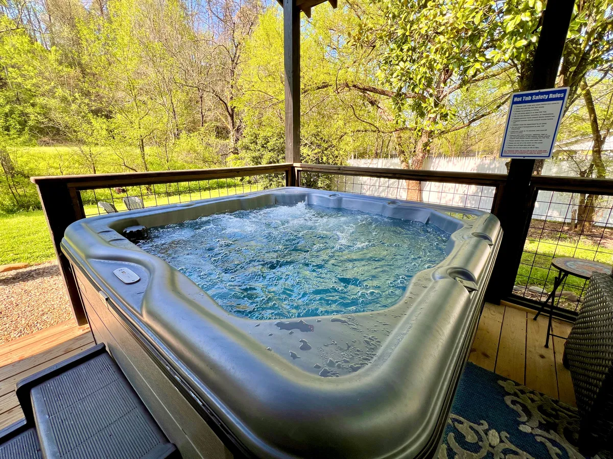 This exterior image captures a private hot tub set against a backdrop of lush Smoky Mountain greenery. The setup evokes a sense of secluded luxury, perfect for unwinding after a day of adventure. The deck area is tranquil and inviting, ideal for morning coffee or stargazing at night.