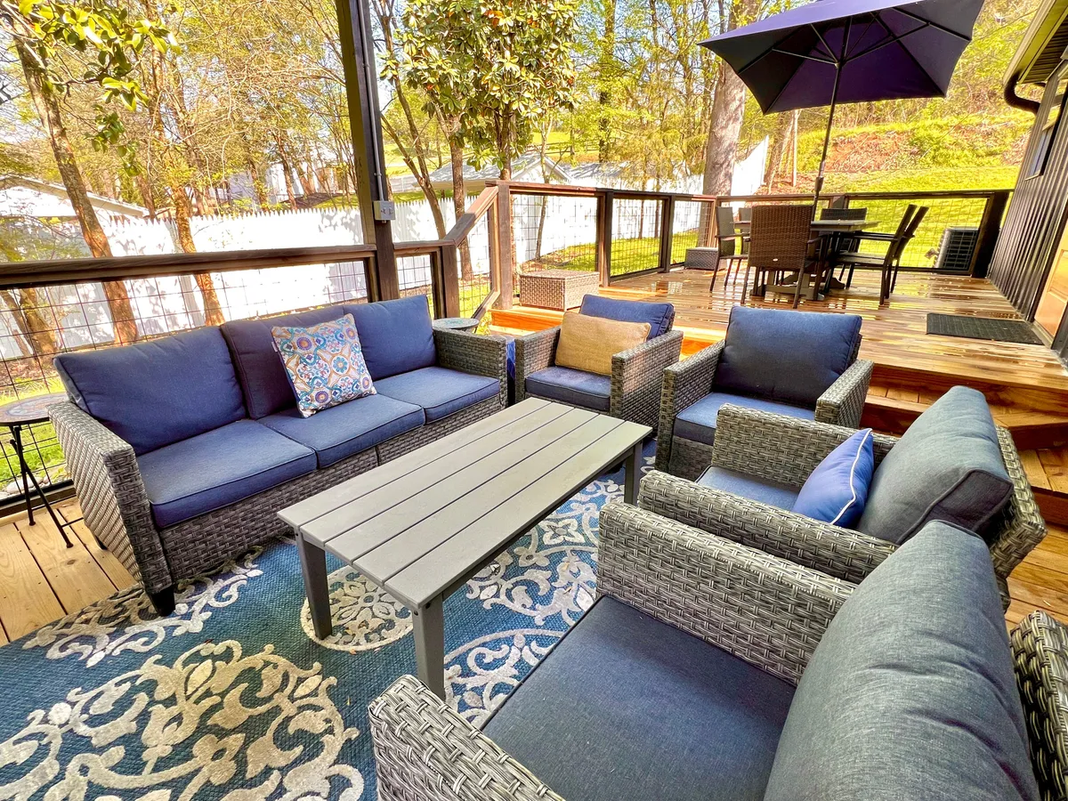 This image displays a comfortable outdoor seating area with throw pillows, a stylish coffee table, and an outdoor dining setup, set against a backdrop of trees. It exudes a cozy, social vibe, perfect for morning coffees or evening relaxation after a busy day of activities.